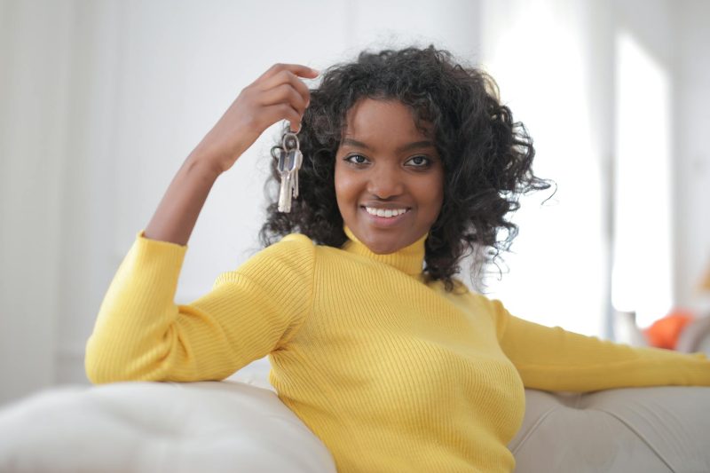 Smiling African American woman holding house keys indoors, symbolizing home ownership.