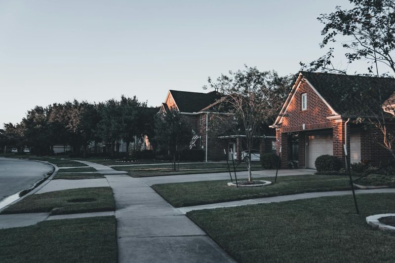 Serene suburban neighborhood at dusk, featuring brick houses and well-maintained landscaped lawns.