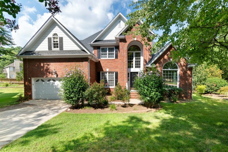 Charming two-story brick house in a sunny suburb with a lush green front lawn.