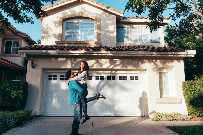 Home 3 Joyful couple embracing in front of their new suburban house on a sunny day.