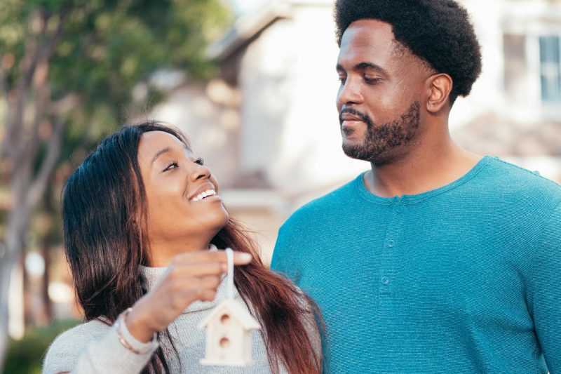 Smiling couple holding a small house model, celebrating their new home ownership.