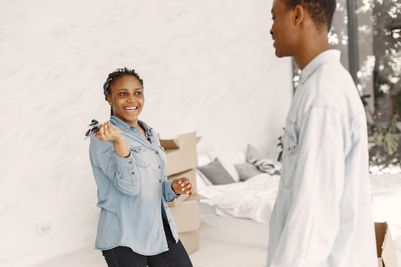 Smiling couple indoors, holding a set of house keys while standing in their new home.
