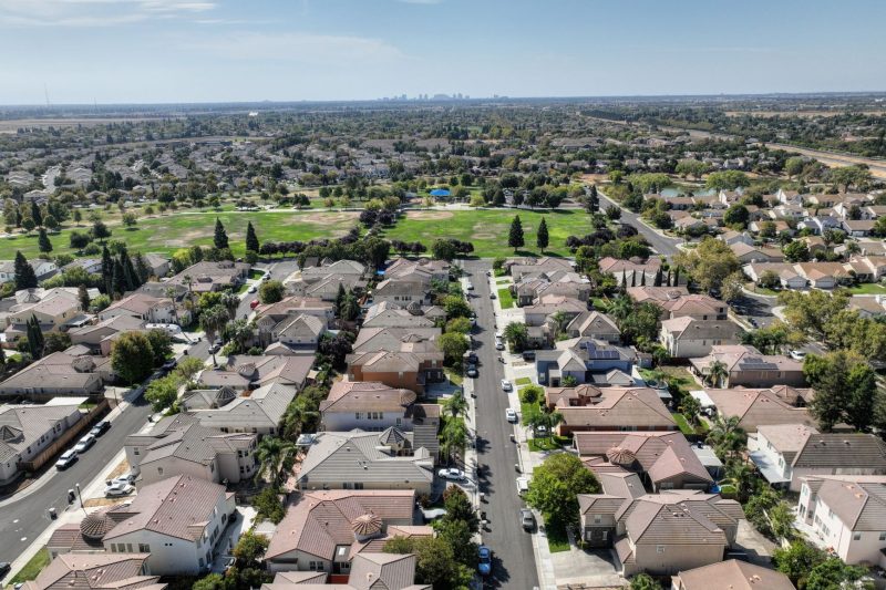 Aerial view of a sunny Sacramento suburb featuring rows of houses surrounded by lush greenery.