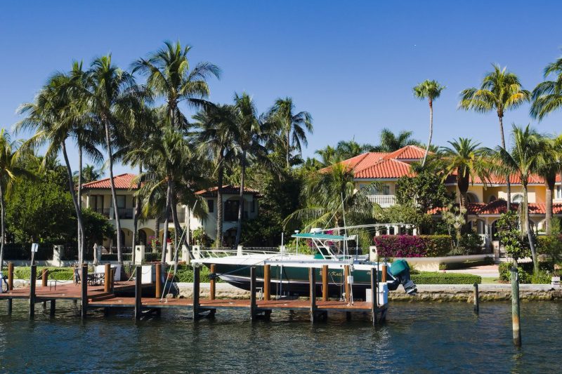 Luxury waterfront homes with palm trees and a boat docked, showcasing a scenic view in Fort Lauderdale, Florida.