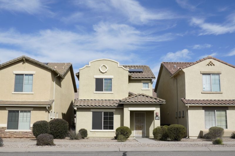 Home 3 Three suburban houses side by side in Tucson, Arizona, under a bright blue sky.